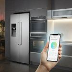 A modern kitchen with smart appliances, including a smart refrigerator with a touch screen display, a smart oven with voice control, and a smart dishwasher connected to a smartphone app for remote monitoring, all seamlessly integrated and controllable through the smartphone app.